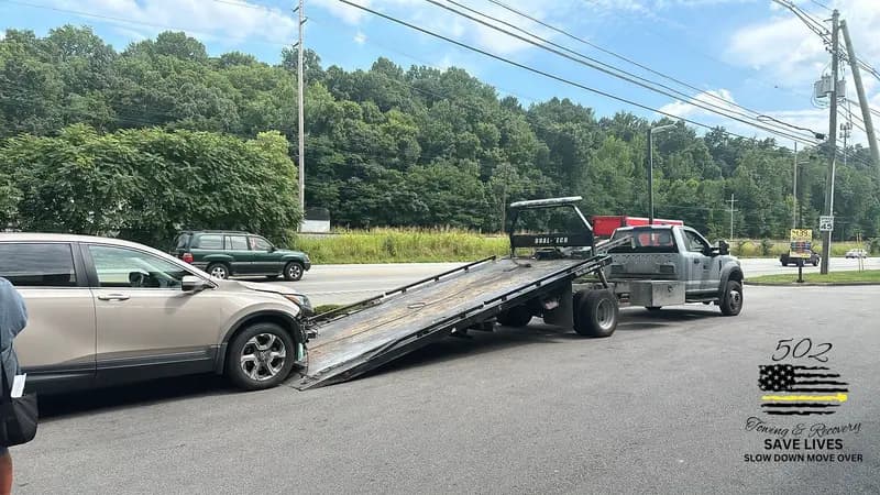A sedan loaded on a flatbed beside the highway